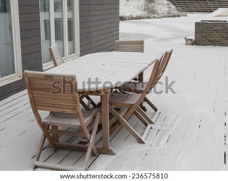 summer wooden table and chairs are covered with snow in winter on the veranda (suddenly summer is ended)