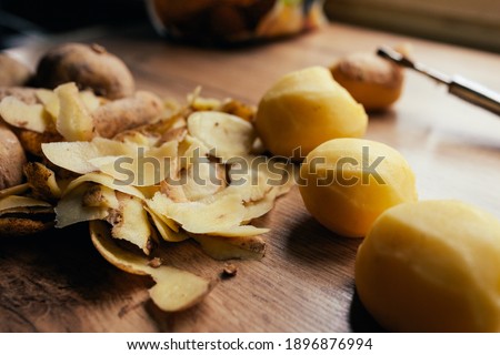 Three russet potatoes peeled and ready for cooking, with leftover peels on the table by the window