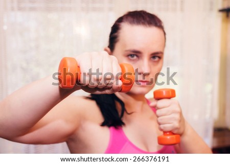 Woman with orange weights in hands in fighting stance.