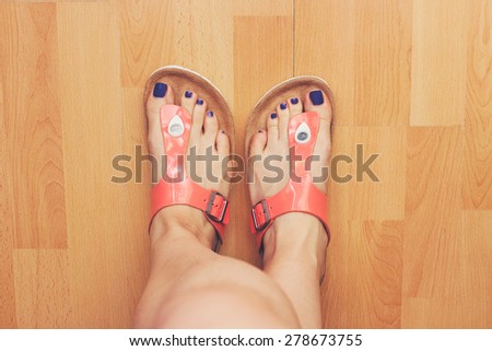 Orange flip flops on female feet with purple nail polish on toes.