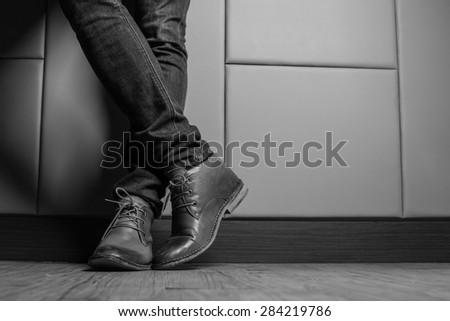 Black and White  Young fashion man\'s legs in blue jeans and brown boots on wooden floor