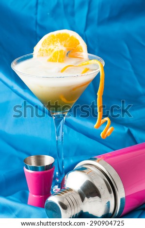 glass of alcoholic drink cocktail with orange slices, cubes and shaker rose on blue