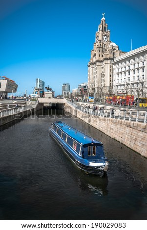 A narrowboat crusing along the Liverpool central canal link at Pier Head with the Liver Building and ferry terminal in the background.
