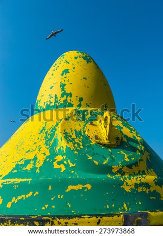 A  weathered buoy for ship navigation out at sea with seagulls overhead.