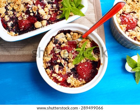 Bowl of crumble with strawberries, red currants, blueberries and blackberries with crumb made of powdered sugar, almonds, flour and oatmeal flakes