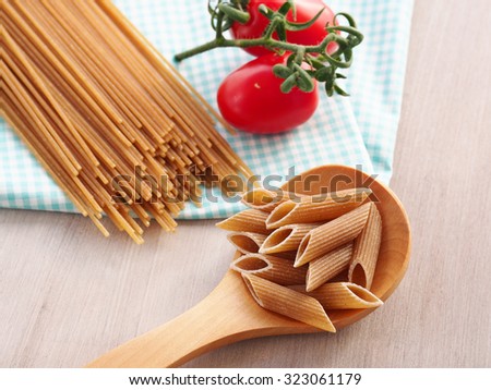 Whole wheat pasta - spaghetti and short pasta penne in wooden spoon on checkered table cloth on wooden table