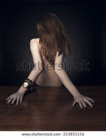 Studio shot. Portrait of model from the back with long curly ginger red hair posing over black background. Long arms, Concept.