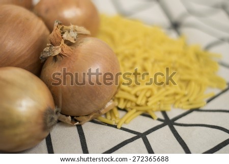 Raw pasta and yellow onions on the fabric under the bright light