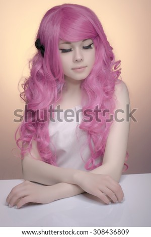 Trendy teenage girl with pink curly hair. Modern young fashionable woman in pastel colors, looking down against pastel pech background.
