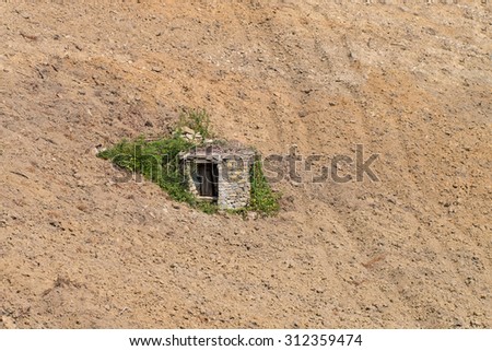 Old well made of stone almost covered by spontaneous vegetation  in a steep plowed field Piedmont Italy