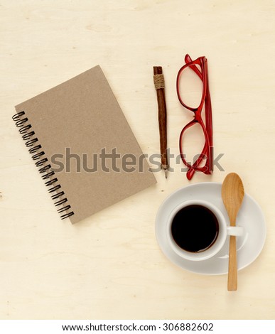 Cup of black coffee, notebook, pen and eyeglass on desk