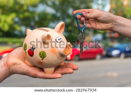 Salesman giving car keys to a new car owner, who is paying all saving money from piggy bank on blurred background