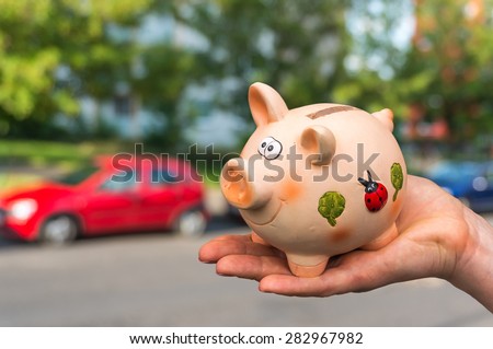All savings money from pink ceramic piggy bank to pay for the dream car on blurred background