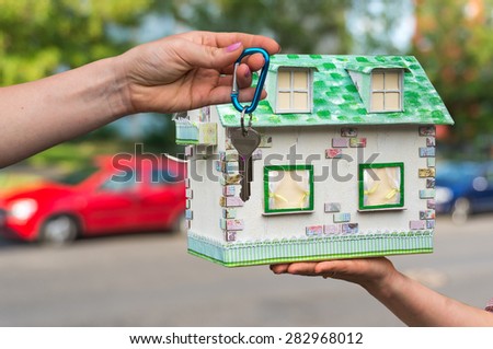 Real estate agent giving house keys to a new property owner, who is holding model house from paper on blurred background