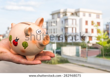 All savings money from pink ceramic piggy bank to pay for the dream house on blurred background