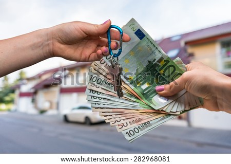 Real estate agent giving house keys to a new property owner, who is paying by euro money on blurred background