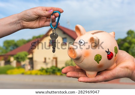 Real estate agent giving house keys to a new property owner, who is paying last saving money from piggy bank on blurred background