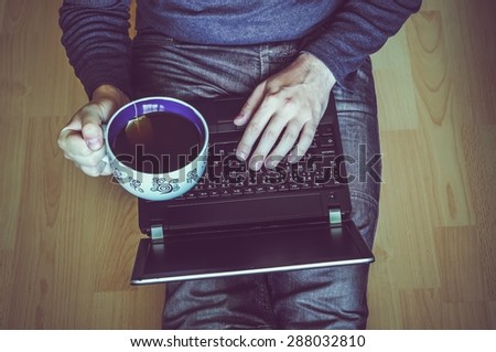 Young student with a cup of tea using a laptop and sitting on the wooden floor in a classroom - retro and vintage style