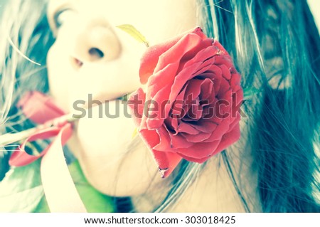 a red rose was carrying at the mouth of a woman , focus at rose more woman ,  cross process effect