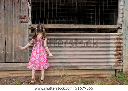 Young inquisitive girl peering into old shed on tiptoes.