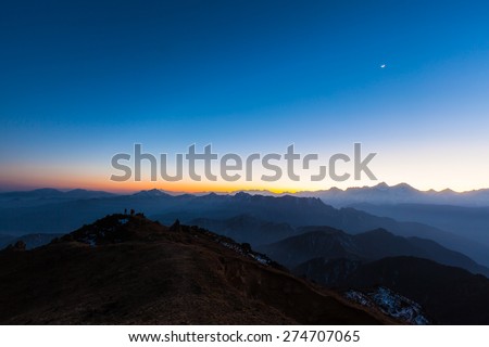 Panorama view of the twilight and moon in the sky with silhouette of mountains and cloudscape on top of Cattle Back Mountain (Niubeishan) in Sichuan Province, China
