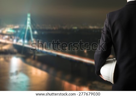 Close up of engineer hand holding white safety helmet for workers security standing in front of blurred urban background.