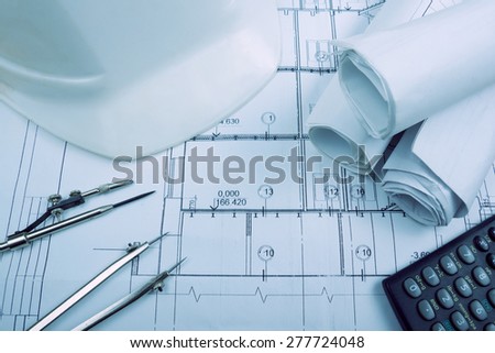 Architectural project, blueprints, blueprint rolls, compass divider, calculator, white safety on plans. Engineering tools view from the top. Copy space. Construction background. Blue toned