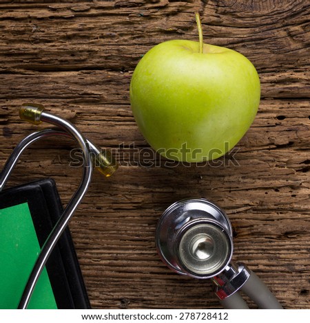 Alternative medicine - stethoscope, clipboard and green apple on wood table top view . Medical background. Concept for diet, healthcare, nutrition or medical insurance