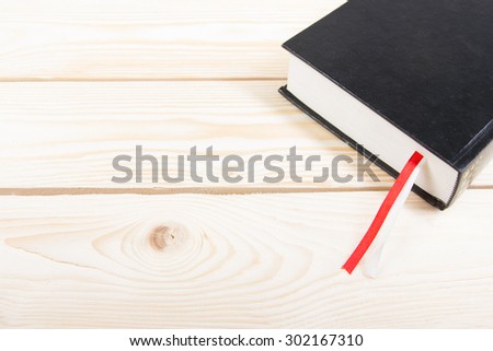 Black book with red and white bookmark on wooden table. Back to school. Copy space