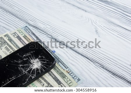 Modern broken mobile phone and money on white wooden background. Copy space. Top view