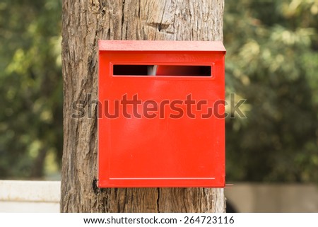 Red   letter  box   fixed   on  trunk  of   big  brown   tree  waiting   for   letter   from   the   postman  in  stead   of   sending   via  e-mail   or   a  new   technology.