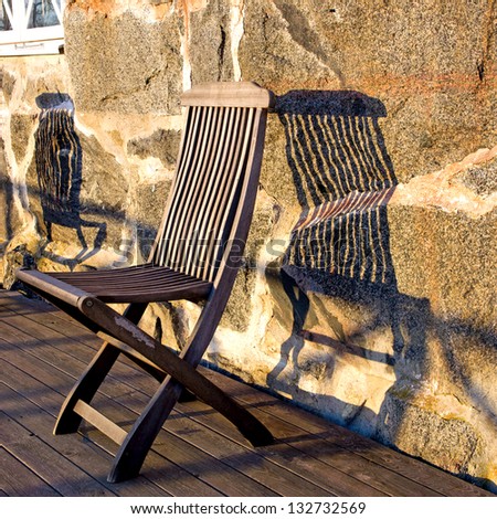 wooden chair on porch casting shadow on stone wall
