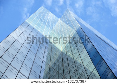 Low angle view of glass facade of tall office building on blue sky