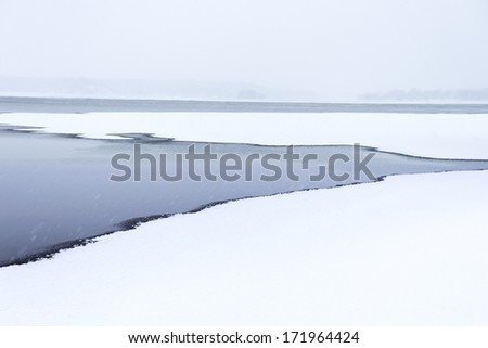 Lake in winter, partly covered in ice, on snowy winter day