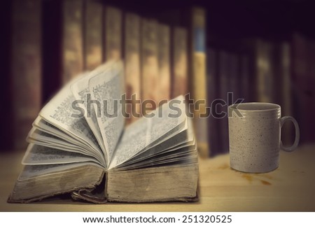 Open vintage books in front of row of other old books, and coffee mug with some spilled coffe on surface