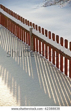 Red wooden fence making a shadow in snow in evening light