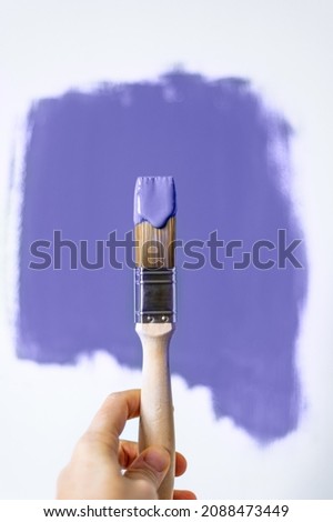 Process of choosing paint for the walls during house renovation, violet very peri color and brush in paint, color of the year 2022