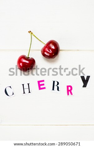 Cherry Letters Cut out from Magazine with Ripe Cherries nearby on White Wooden Background