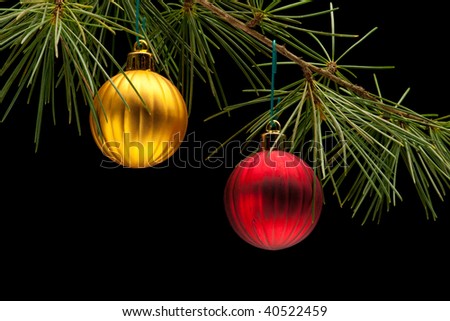 Red and golden matte bauble christmas ornaments on pine tree branch. Black background. Horizontal composition.