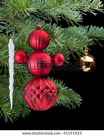 Snowman made from red baubles holding white icicle christmas ornament on fir tree branch. Black background. Vertical composition.