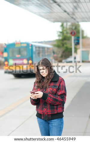 Young girl texting on bus stop. Shallow depth of field.