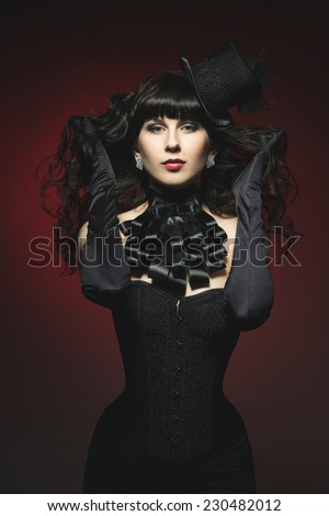 Beautiful fantasy gothic vampire brunette woman in sexy black satin corset, burlesque hat, jabot and long gloves