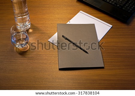 Notepad, file, pencil, bottle, glass of water and laptop on a wooden desk