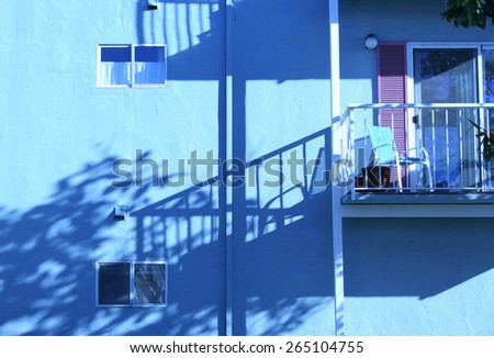 Balcony casting long shadows, blue building, California coast.
