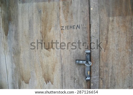 The German word ziehen, or pull, written on an old weathered wooden door with a black metal latch.