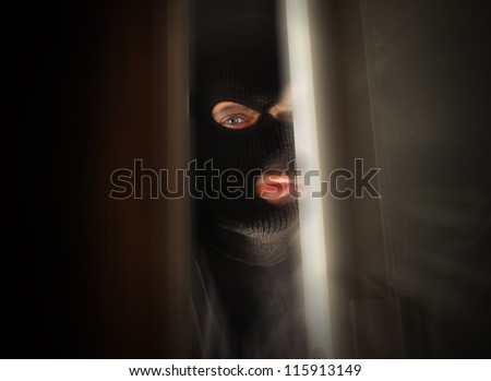 A man with a black mask is breaking into a home and the focus is in his eye. Use it for a security or danger concept.