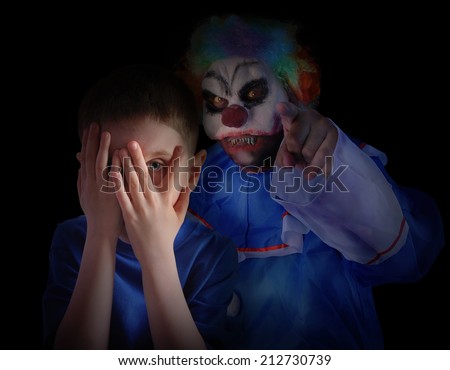 A child is hiding his eyes in the dark night and looks scared and upset at creepy clown. The boy is isolated on a black background for a fear concept.
