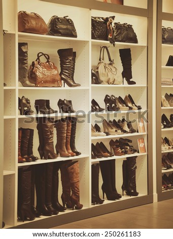 A variety of boots and purses are on display at a store on white shelves for sale. Use it for a shopping or fashion concept.