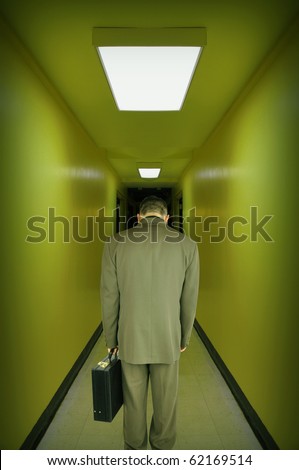 A tired, overworked, stressed business man is walking down a green tint hallway with his head down. Use it for a powerlessness, employment or worry concept.