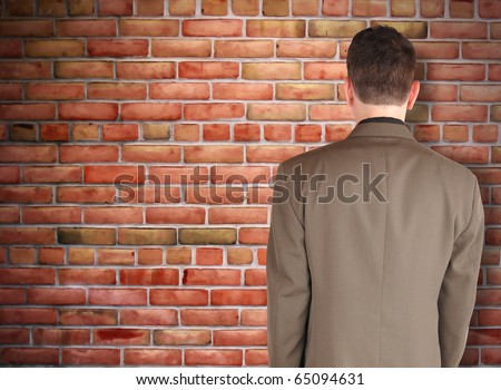 A business man has his back turned and looking at a brick wall. Can represent an obstacle, sadness or a struggle.